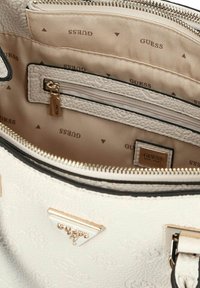 Borsa Guess bianca texture con zip aperta che mostra l'interno in tessuto beige con logo e una tasca interna con zip e tirante color oro.