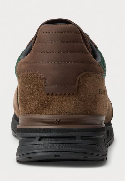 Brown suede sneaker with textured upper, green accents, and a padded heel. Features a black rubber sole with notable stitching details.
