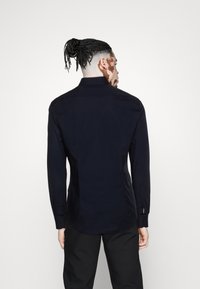 Marineblaues Langarmhemd mit tailliertem Schnitt, Knopfmanchetten und klassischem Kragen. Glatte Textur mit einem sauberen Finish über den Rücken.