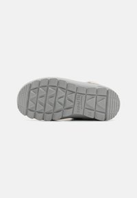 Suela de zapato de goma gris con un patrón de textura en la suela y un logo elevado. Las características incluyen ranuras triangulares para agarre y flexibilidad.