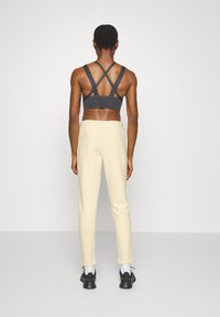 Top deportivo gris con tirantes cruzados, combinado con pantalones de chándal color crema. Los pantalones cuentan con una cintura con cordón y piernas ajustadas. Unos zapatos negros completan el look.