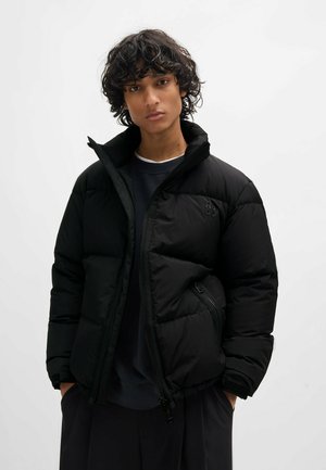 Black puffer jacket featuring quilted sections, high collar, and zippered pockets. Made of smooth fabric with a matte finish.
