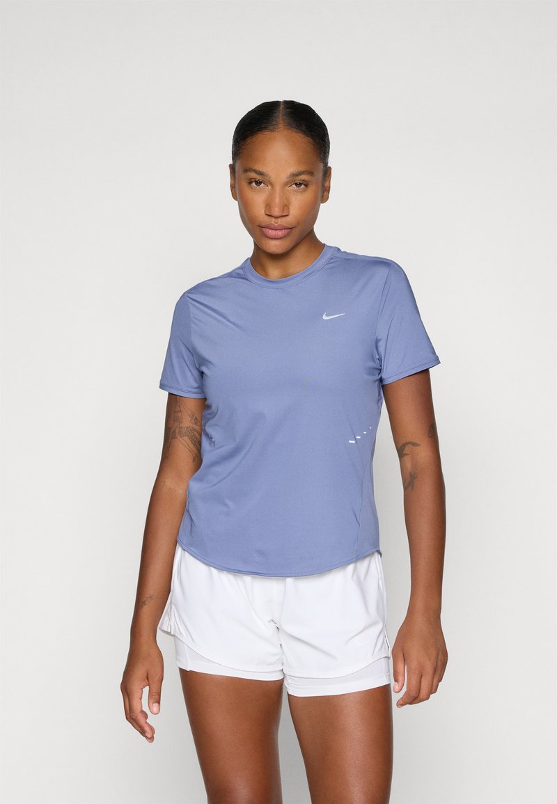 T-shirt de sport Nike en violet clair, à manches courtes, avec un col rond ; associé à un short blanc. Présente un petit logo sur la poitrine.
