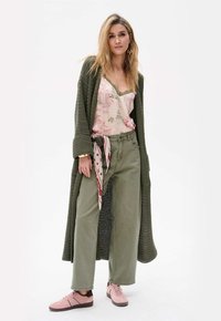 Groene gebreide cardigan, bloemen tanktop, olijfgroene wijde broek, patroon sjaal, roze sneakers; gestructureerde materialen en een ontspannen silhouet.
