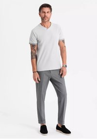 Lys grå bomulds v-hals t-shirt parret med grå skræddersyede bukser og sorte slip-on sko, med opfoldede ærmer og tatoveringer synlige på armene.