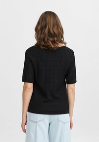 Sort ribbet striktop med korte ærmer, bred halsudskæring, tekstureret overflade og tætsiddende talje. Båret sammen med lyseblå baggy jeans.