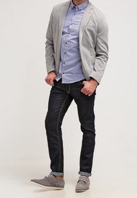 Šedé sako přes světle modrou pruhovanou košili, tmavé džíny se žlutým prošitím a šedé boty se světlými podrážkami. Neformální, ale upravený vzhled.