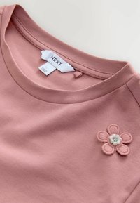 Rosa Kurzarm-T-Shirt mit rundem Halsausschnitt und einer gestickten Blumenapplikation mit Perlen, aus weichem Baumwollstoff gefertigt.