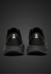 Para czarnych butów sportowych z grubymi szarymi podeszwami, widocznych od tyłu, z trzema poziomymi odblaskowymi paskami na każdym pięcie.