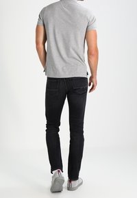 Polo grigio a maniche corte abbinato a jeans scuri. La maglietta presenta un colletto, mentre i jeans hanno una vestibilità slim e tasche posteriori discrete.