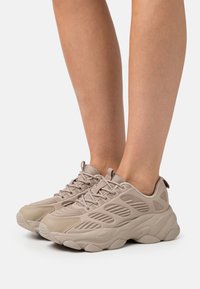 Scarpe sportive beige con una tomaia in rete testurizzata, colletto imbottito e una suola in gomma spessa dotata di scanalature per la trazione.