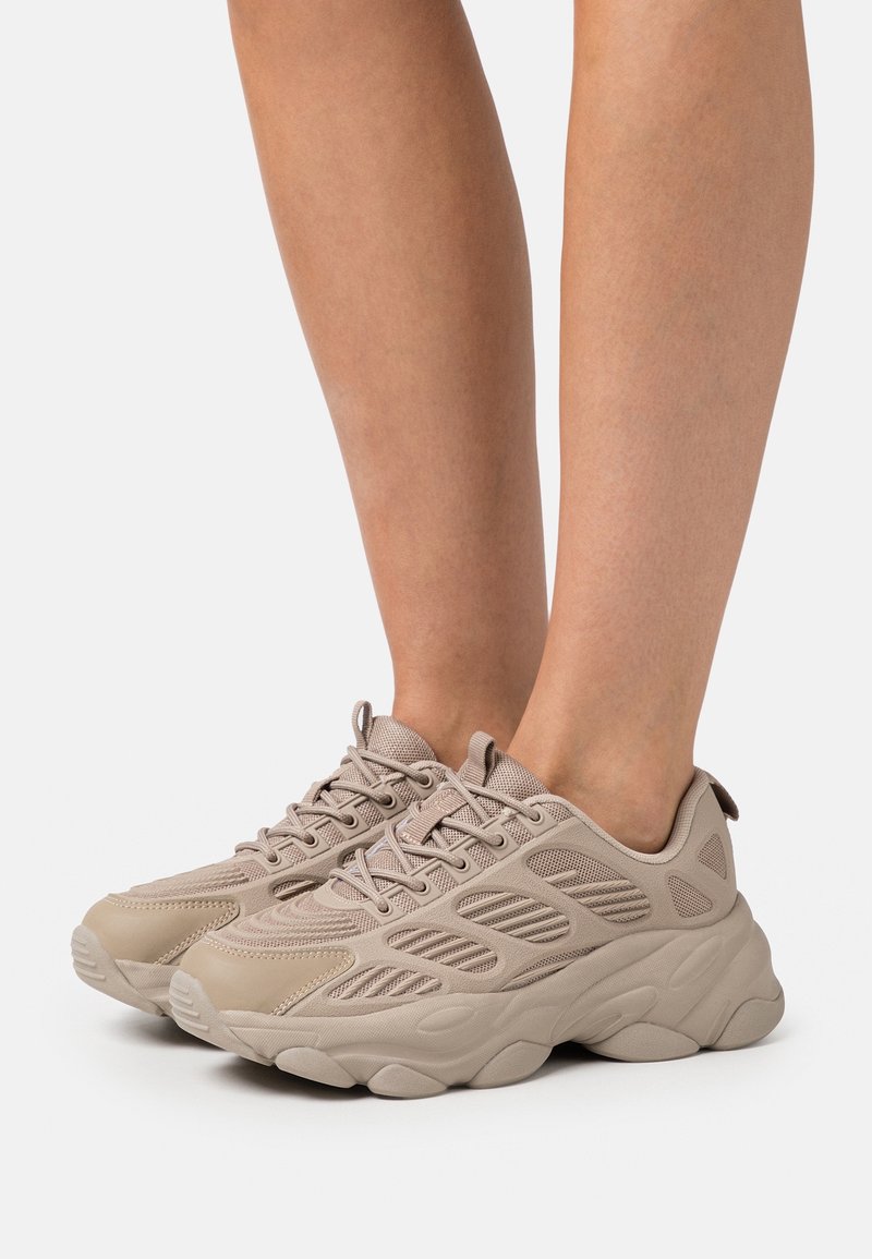 Scarpe sportive beige con una tomaia in rete testurizzata, colletto imbottito e una suola in gomma spessa dotata di scanalature per la trazione.