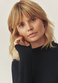 Námornícka dlhá rukávová blúzka s priliehavým strihom; mäkká tkanina s rolovanými manžetami. Modelka s stredne blond vlasmi, s jemným make-upom, priamo sa pozerajúca do kamery.