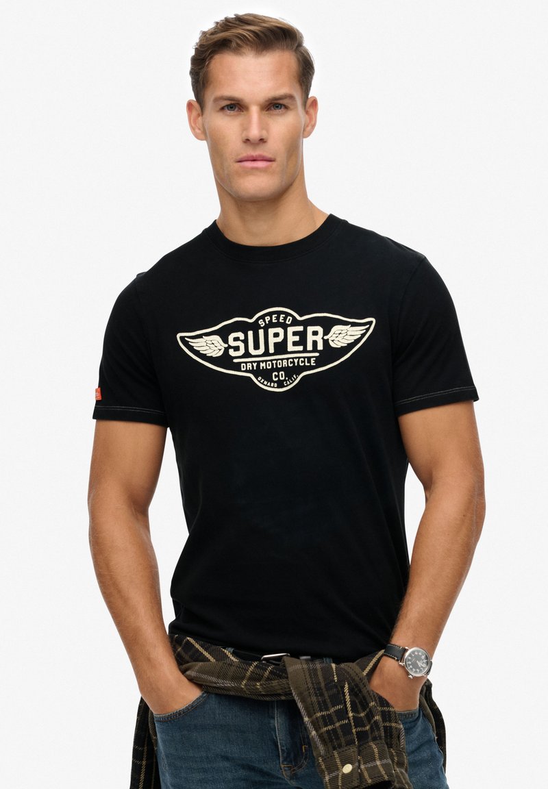 Zwarte katoenen T-shirt met een crèmekleurige grafiek van vleugels en het woord "SUPER" in het midden. Fitted design, korte mouwen en ronde hals.