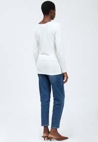 Hvid langærmet skjorte med ribbet tekstur, rund halsudskæring, parret med blå denimjeans i tætsiddende pasform og brune lave hæle.