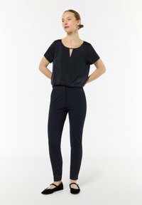 Czarna satynowa bluzka z krótkim rękawem i wycięciem w kształcie łezki, zestawiona z obcisłymi granatowymi spodniami i czarnymi balerinami. Prosty, dopasowany design.