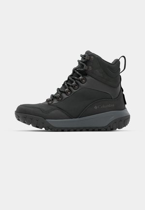 Bota de senderismo negra impermeable con diseño de tobillo alto, suela de goma, ojales reforzados y soporte texturizado para el tobillo. Logo de Columbia en el lado.