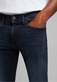 Mörkblå denimjeans med en figursydd design, som har en klassisk femficksstil och metallknäppning, glatt material.