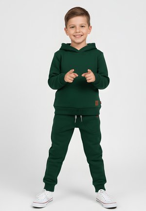 Zielona bluza z kapturem oraz dopasowane spodnie dresowe, wykonane z miękkiego materiału. Posiadają przednie kieszenie, ściągacze przy mankietach oraz brązową metkę jako akcent.