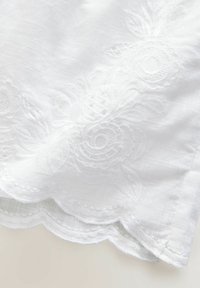 Vit tyg med blommönster broderat, med vågade kanter. Texturen är slät med en lätt glans. Intrikat detaljering på designen.