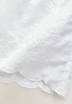 Tessuto bianco con ricami floreali, caratterizzato da bordi scallop. La texture è liscia con una leggera lucentezza. Dettagli intricati nel design.