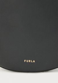 Μαύρη δερμάτινη τσάντα χειρός με απαλό υφή. Διαθέτει χρυσαφένιο ανάγλυφο λογότυπο "FURLA" στο μπροστινό μέρος, κυκλικό σχέδιο και μινιμαλιστικό στυλ.