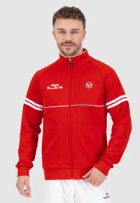 Rote Zip-Jacke aus glattem Stoff, mit weißen Streifen über den Schultern, einem hohen Kragen und gestickten Logodetails.