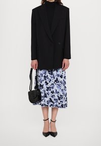 Černý oversized blazer přes přiléhavý černý top, doplněný modrou a bílou sukní s abstraktním potiskem. Černá kabelka a špičaté lodičky.