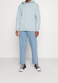 Sudadera con capucha azul claro con un bolsillo tipo canguro, combinada con vaqueros de pierna ancha azul claro y zapatillas altas negras. Conjunto casual.