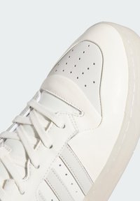 Białe sneakersy z gładką skórzaną cholewką, miękkimi szarymi akcentami, perforowanymi detalami i płaskimi sznurowadłami na teksturowanym wzorze.