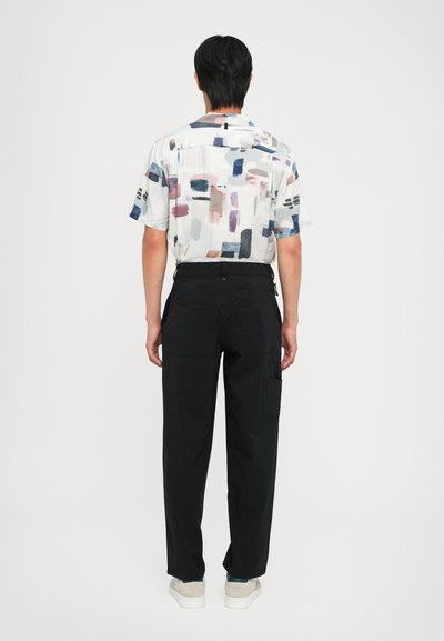 Camisa de manga corta en tejido ligero con un patrón abstracto colorido; combinada con pantalones cargo negros que tienen bolsillos laterales y un diseño de pierna recta.