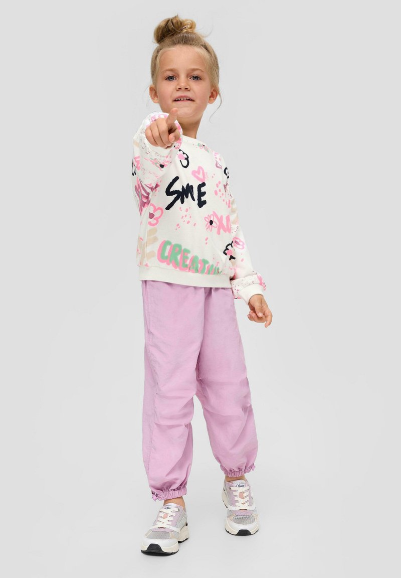 Tenue pour enfants comprenant un pull à motifs colorés avec des accents roses, noirs et verts, associé à un pantalon de jogging rose pâle et des baskets sportives.