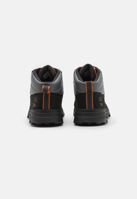 Czarne i szare wysokie buty sportowe z pomarańczowymi akcentami, posiadające teksturowany zamsz i gładki syntetyczny wierzch, oraz solidną czarną gumową podeszwę.