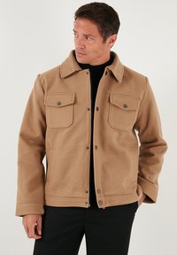 Brązowa kurtka z mieszanki wełny, z zapięciem na guziki, dwoma kieszeniami na piersiach i spiczastym kołnierzem. Charakteryzuje się miękką fakturą i luźnym krojem.