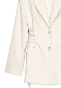 Blazer de marfil hecho de una tela suave, con solapa en pico, dos botones y detalle de cordones a lo largo del costado con lazos a juego.