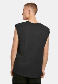 Tricou negru supradimensionat fără mâneci, cu gât rotund, textură fină și o croială lejeră. Pe spate are un design simplu, fără logo-uri vizibile.