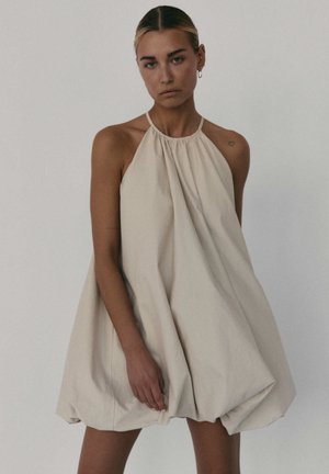 Jasno beżowa sukienka na ramiączkach z marszczoną linią dekoltu i luźnym krojem. Wykonana z miękkiego materiału, z zaokrąglonym dołem i minimalną ilością szwów.