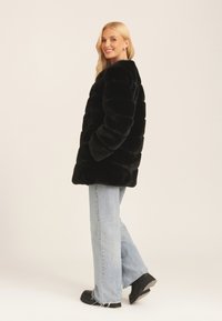 Black faux fur coat with a puffy design, featuring a rounded neckline and wide sleeves, paired with light blue flared jeans and black boots.