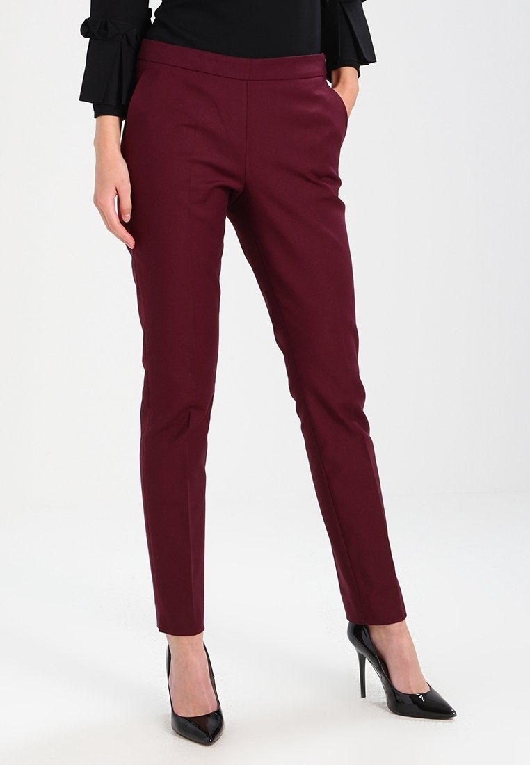 Femme portant un pantalon slim bordeaux avec poches et des chaussures à talons noirs, associé à un haut noir avec des manches à volants.