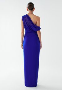 Viena pleca, līdz zemei garš kleita spilgtā zilā krāsā. Raksturīga drapēta auduma detaļa uz pleca, pieguloša silueta un mīksts materiāls.