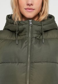Khaki zielona kurtka puchowa z zamkiem błyskawicznym, regulowanym kapturem na sznurki i pikowanym wykończeniem, prezentująca gładką, błyszczącą powierzchnię.
