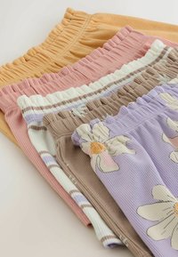 Pile de cinq shorts en tissu côtelé avec ceintures élastiques à la taille, en jaune pastel, rose, blanc rayé, marron avec des fleurs, et lavande avec de grandes fleurs.