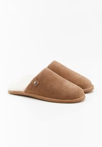 Pantofole in suede marrone con un morbido rivestimento in pelliccia bianca, punta arrotondata e un piccolo bottone d'accento argentato sul lato. Design con suola piatta.