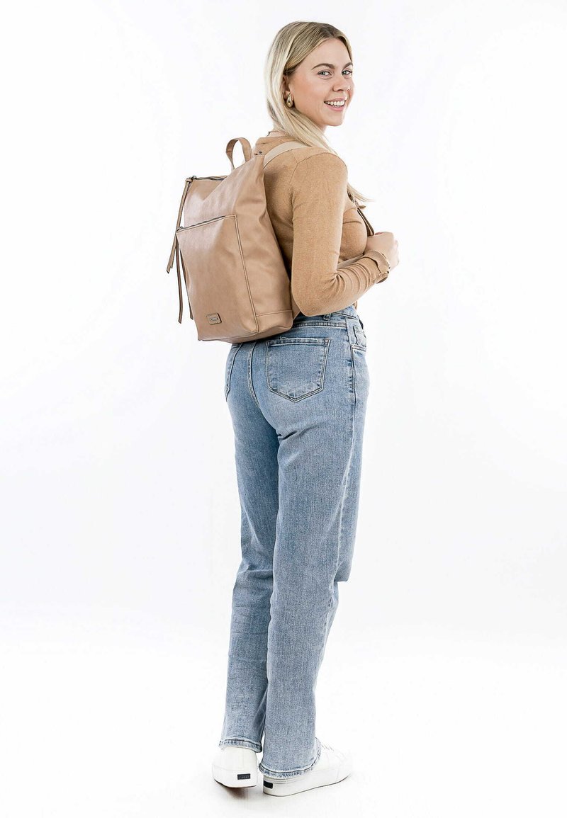 Zaino in pelle beige chiaro con chiusura a zip, tasca frontale piatta, spallacci imbottiti, forma rettangolare e superficie liscia, indossato da una persona.