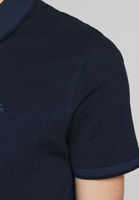 Mörkblå polo skjorta med texturerad tyg, korta ärmar med kontrasterande kant och en klassisk kragdesign.