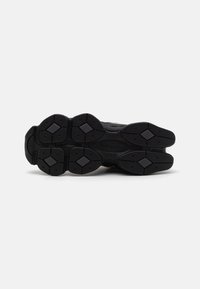 Semelle noire de sneaker vue de dessus, présentant une bande de roulement segmentée avec des formes losanges et le logo "new balance" au centre.