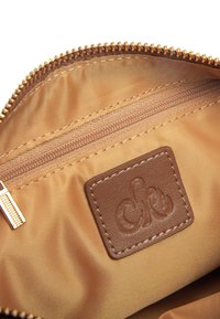 Interno di una borsa in nylon marrone con una cerniera dorata, dotata di una tasca separata con cerniera e di un'etichetta in pelle con logo impresso sul rivestimento.
