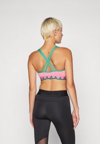Adidas sportbh med rosa bunn, teal korsryggstropper og svart geometrisk mønster. Materialet ser ut til å være elastisk; kombinert med svarte leggings.
