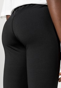 Leggings pretos com um tecido liso e elástico; design ajustado que mostra os contornos; apresenta uma cintura alta para maior conforto.