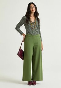 Pantaloni verdi a gamba larga abbinati a una blusa a fantasia nei toni del verde, nero e bianco. Gli accessori comprendono una collana a più fili e una borsa bordeaux.